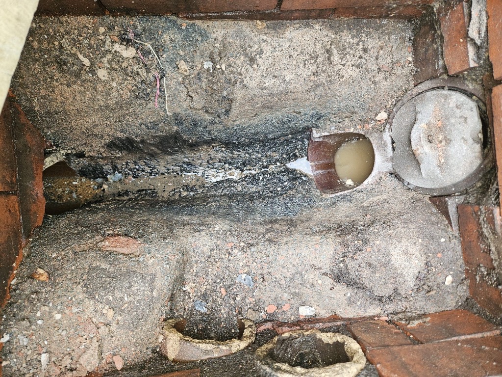 Damaged manhole with no drainage channel and rough concrete base causing blockages